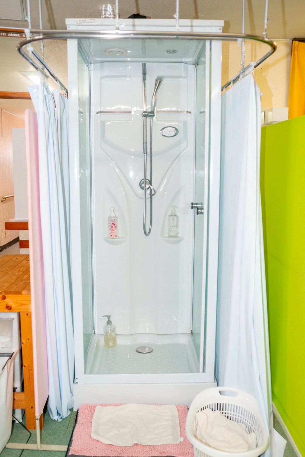 A shower enclosure with a glass door, a handheld showerhead, and a bottle of soap.