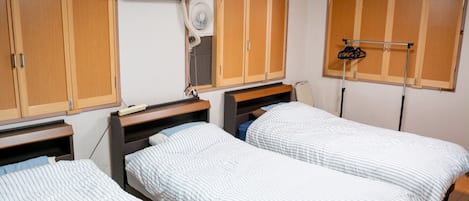 A bedroom with two single beds, wooden wardrobes, a ceiling fan, and a window with a curtain.