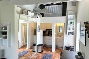 Une cuisine compacte dotée d’un ventilateur de plafond, un coin repas avec une table et un petit espace salon avec une chaise.