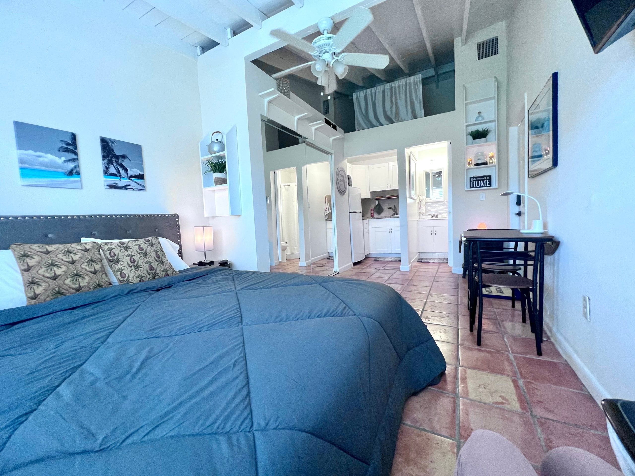 Quarto com cama grande, escrivaninha e vista para a cozinha e banheiro.