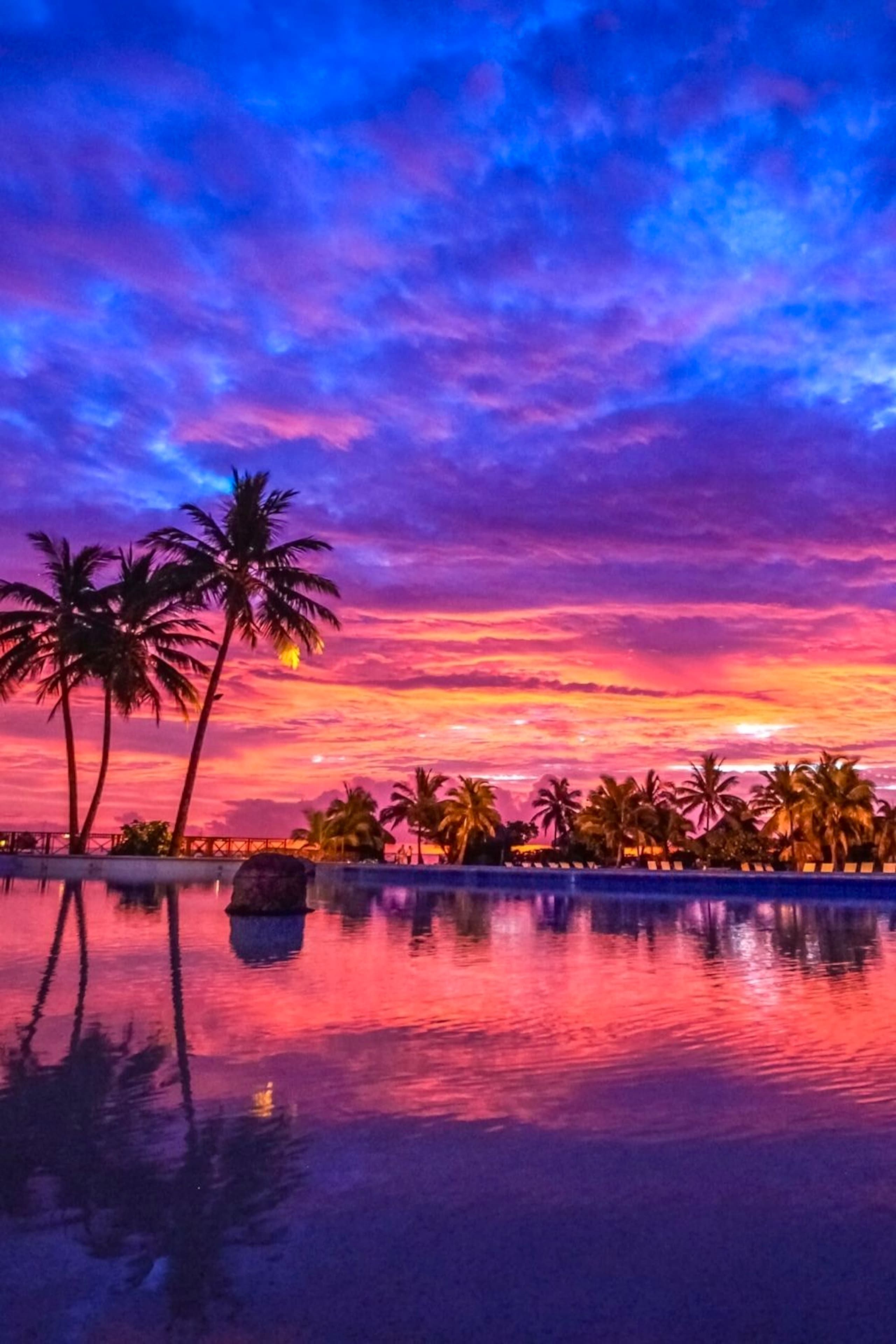Atardecer sobre un cuerpo de agua con palmeras y el reflejo del cielo.