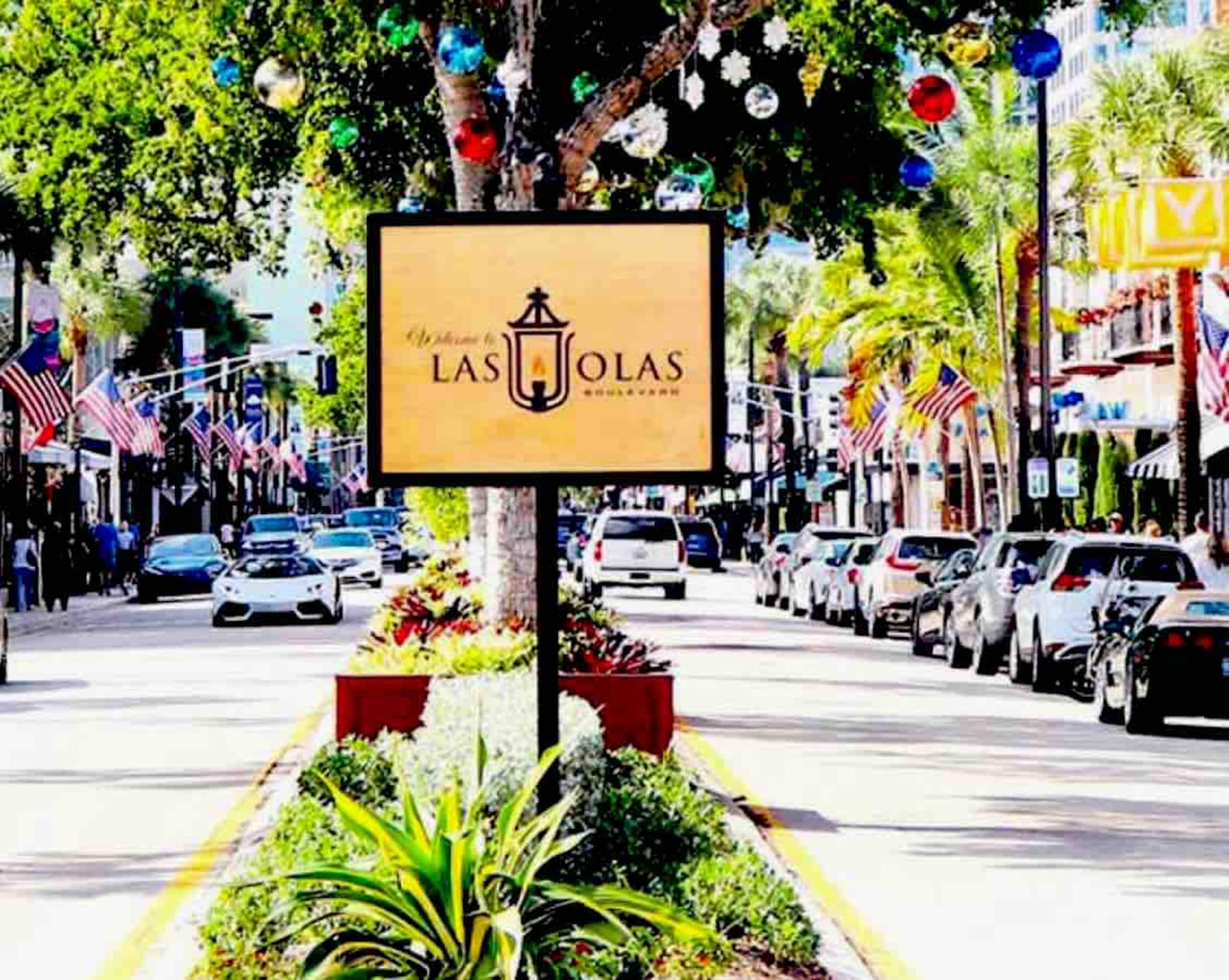 A street view with a sign for 'Las Jolas' hotel, lined with parked cars and American flags.