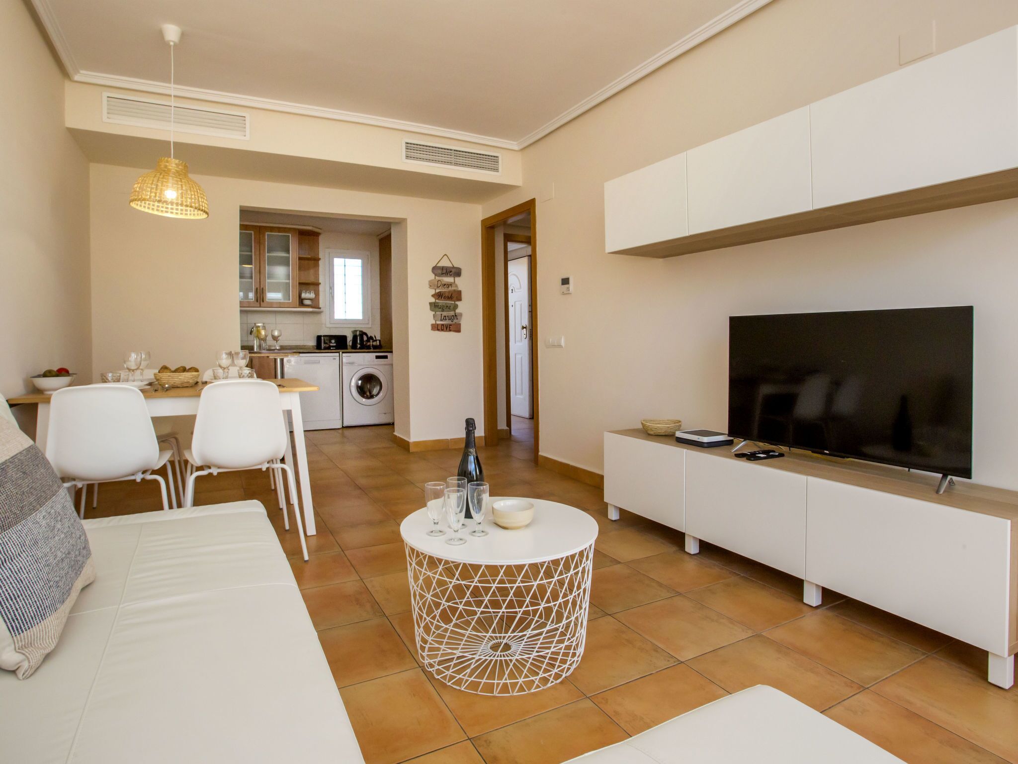 A modern living room with a sofa, a dining area, a kitchen, and a TV on a stand.