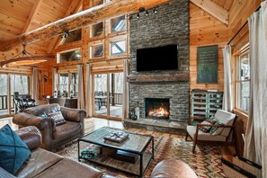 A cozy cabin interior with a stone fireplace, leather furniture, and large windows.