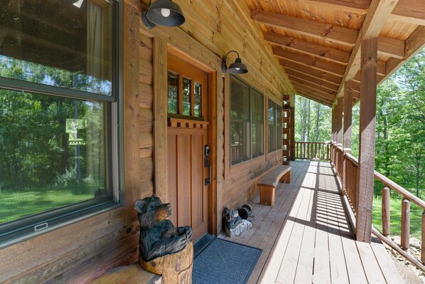 A wooden cabin with a covered porch, large windows, and a bench.
