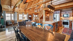 Un intérieur de cabane en bois spacieux, comprenant un coin repas, une cuisine et un escalier menant à un niveau supérieur.