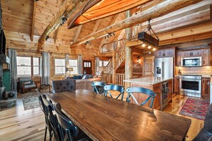 A spacious wooden cabin interior with a dining area, kitchen, and a staircase leading to an upper level. - Rising Ridge Lodge | Hocking Hills, 12 Acres (Logan)