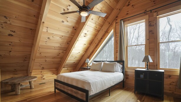 Une chambre à coucher avec un plafond en pente, un lit, une table de chevet, une lampe et une fenêtre.