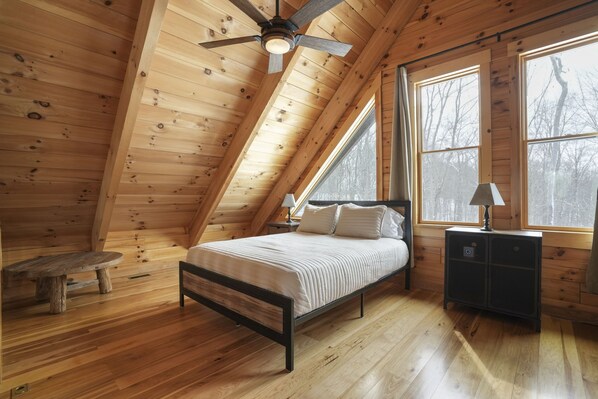A bedroom with a sloped ceiling, a bed, a nightstand, a lamp, and a window.