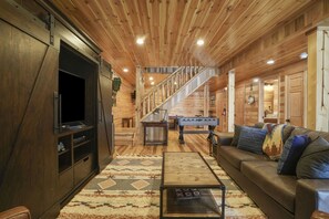 A wooden interior with a staircase, a sofa, a coffee table, and a television.