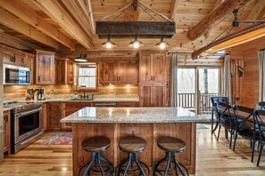 A wooden cabin interior with a kitchen featuring a granite countertop, stainless steel appliances, and a bar area with stools. - Rising Ridge Lodge | Hocking Hills, 12 Acres (Logan)