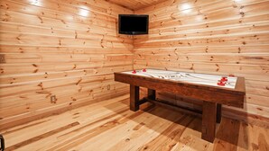Une pièce en bois avec une table de billard et un téléviseur fixé au mur.