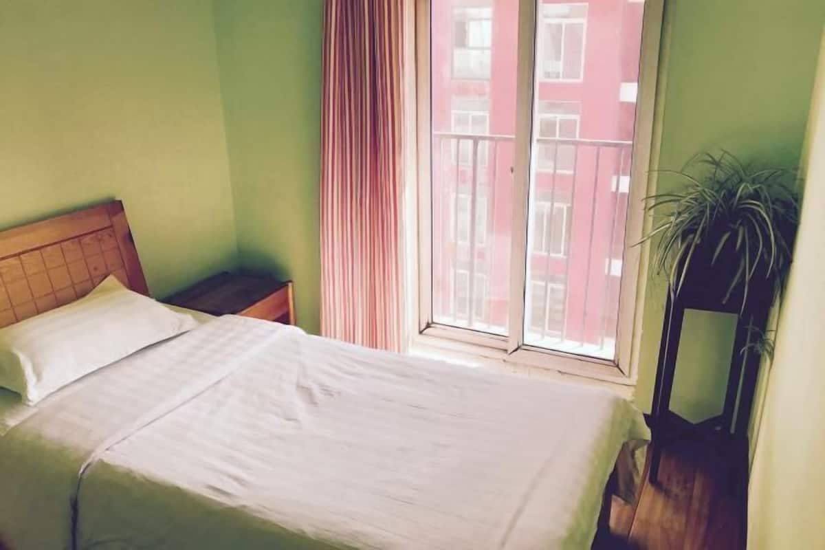 A room with a bed, a nightstand, a window with curtains, and a potted plant.