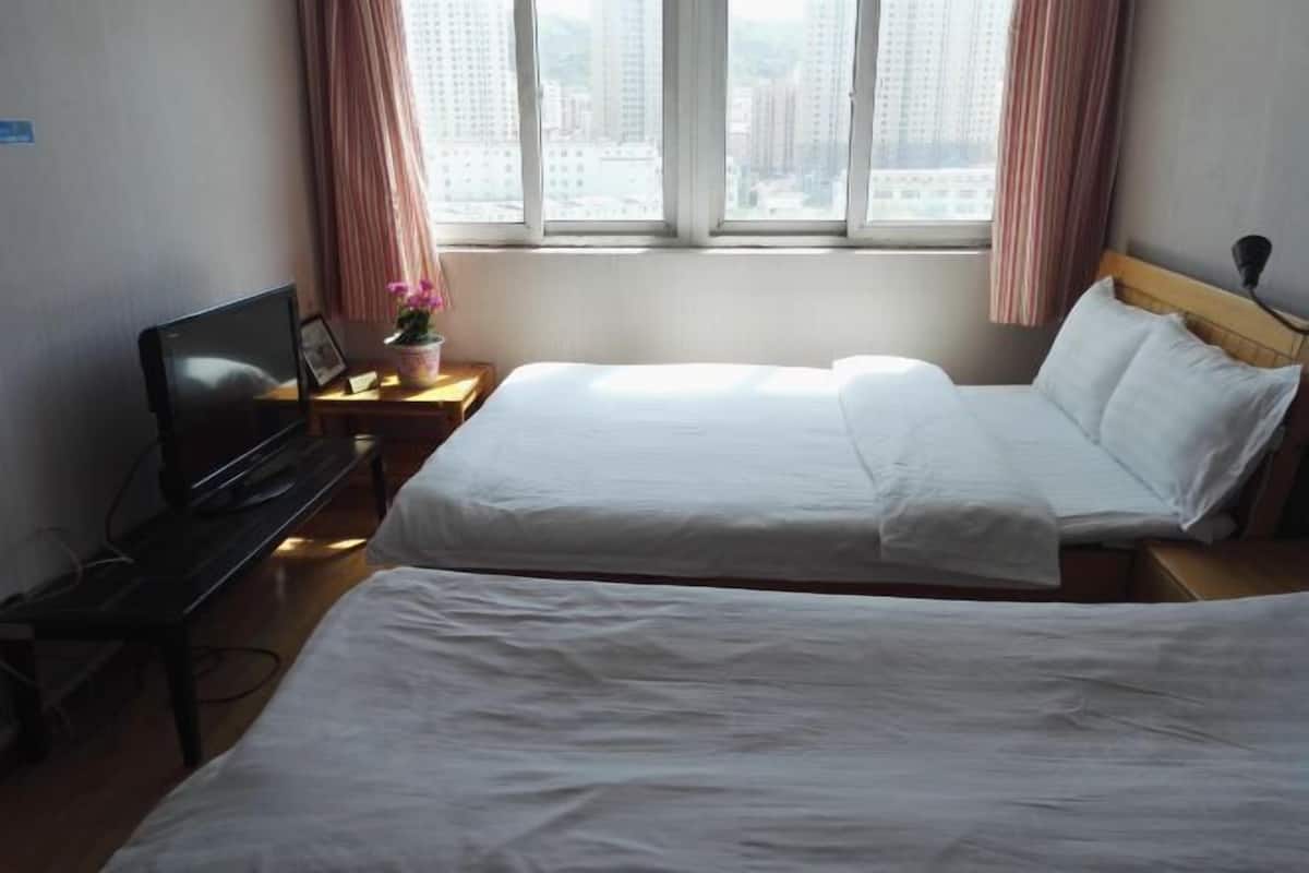 A hotel room with two beds, a desk with a laptop, a TV, and a window with curtains.