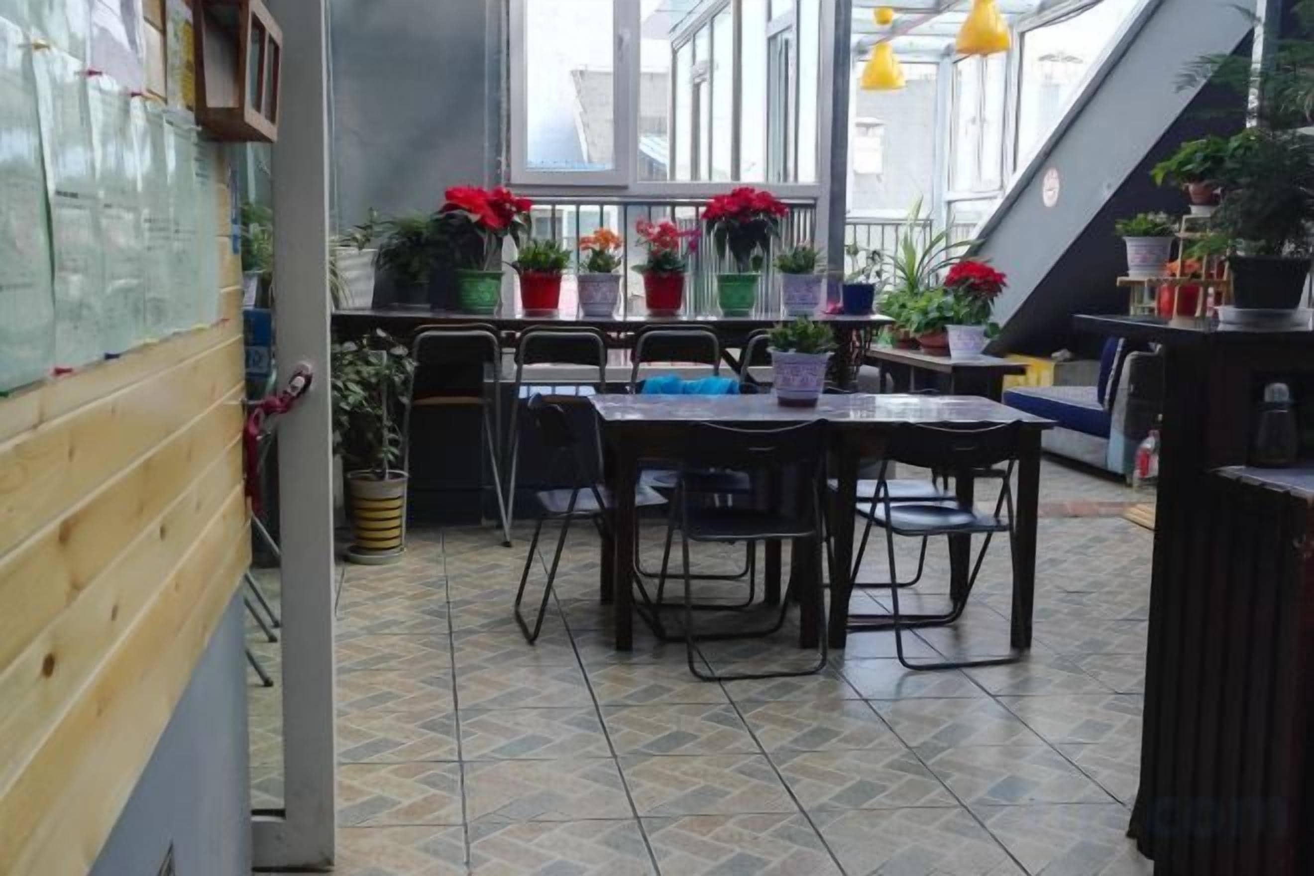 An indoor dining area with a table and chairs, potted plants, and a view through large windows.