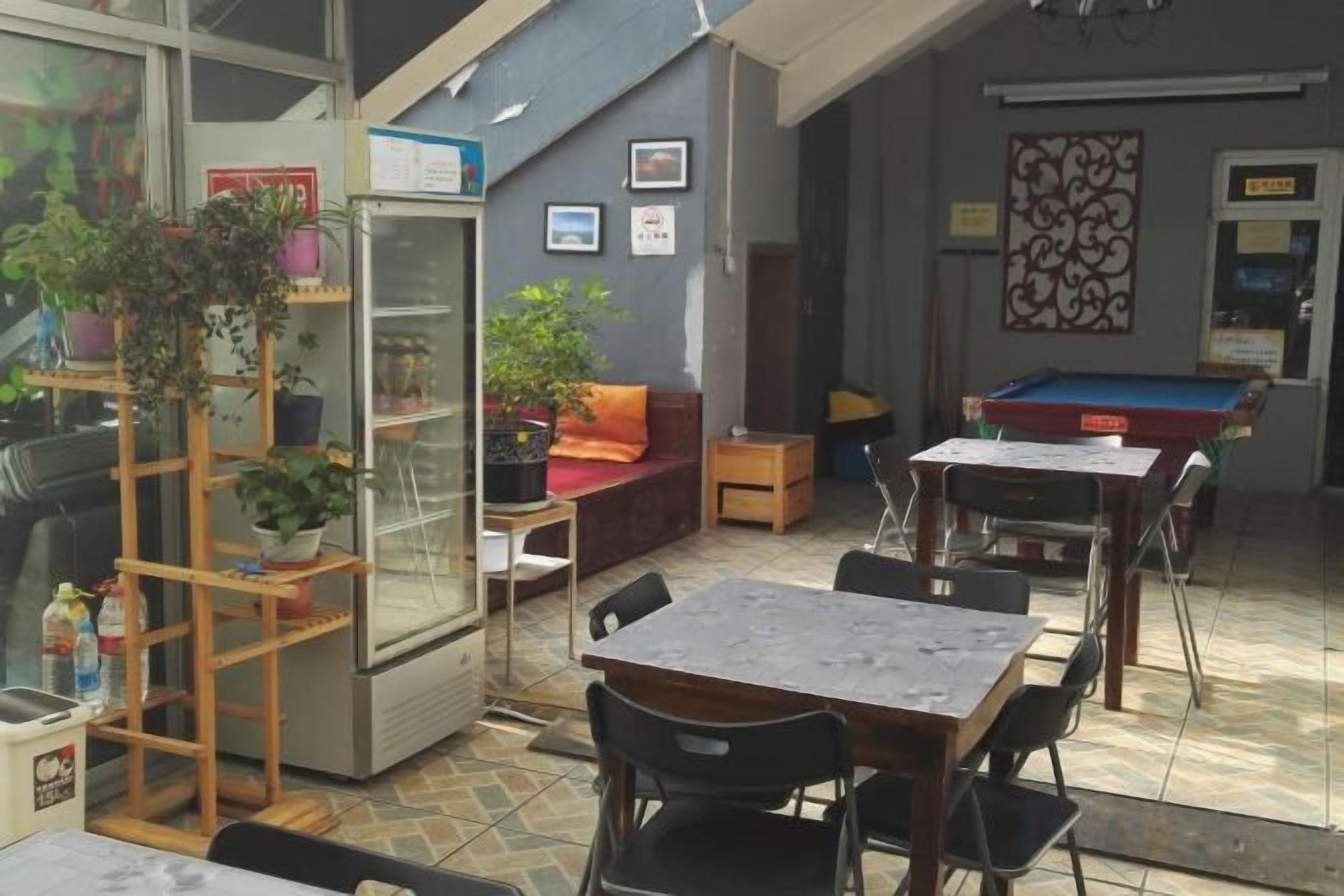 A billiards room with tables, chairs, a refrigerator, and potted plants.