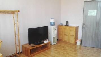 A room with a television on a wooden stand, a water dispenser, a cabinet, and a door with a sign.