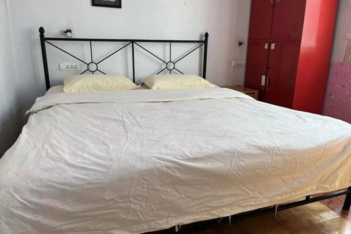 A bed with a metal frame, white bedding, and a red wardrobe in the background.