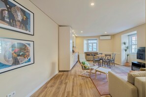 Relax in this stylish living space with a sofa, dining table, and TV, surrounded by artwork and a large window with an outside view.