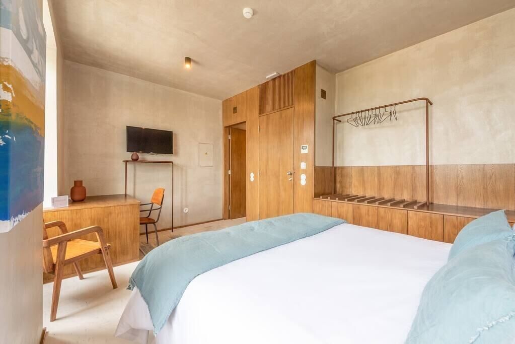 Un dormitorio con cama, armario de madera, escritorio con silla, televisor y un tendedero de pared.