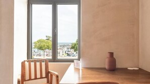 Une pièce avec une table et des chaises en bois, une fenêtre donnant sur un paysage urbain et un vase posé sur la table.