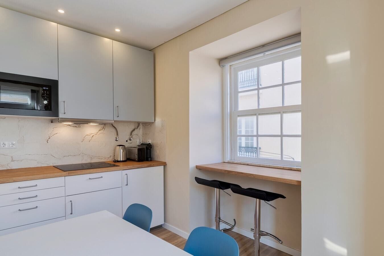 A modern kitchen with white cabinets, a marble backsplash, and a window with a view.