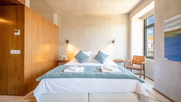 Une chambre moderne avec un grand lit, une armoire en bois, des lampes de chevet et une vue sur la ville par la fenêtre.