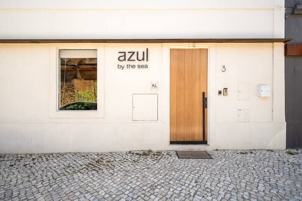 A building facade with a sign reading "azul by the sea," a wooden door, and a cobblestone ground.