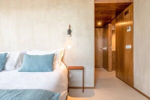 Een slaapkamer met een bed, nachtkastje, wandlamp en een houten deur.