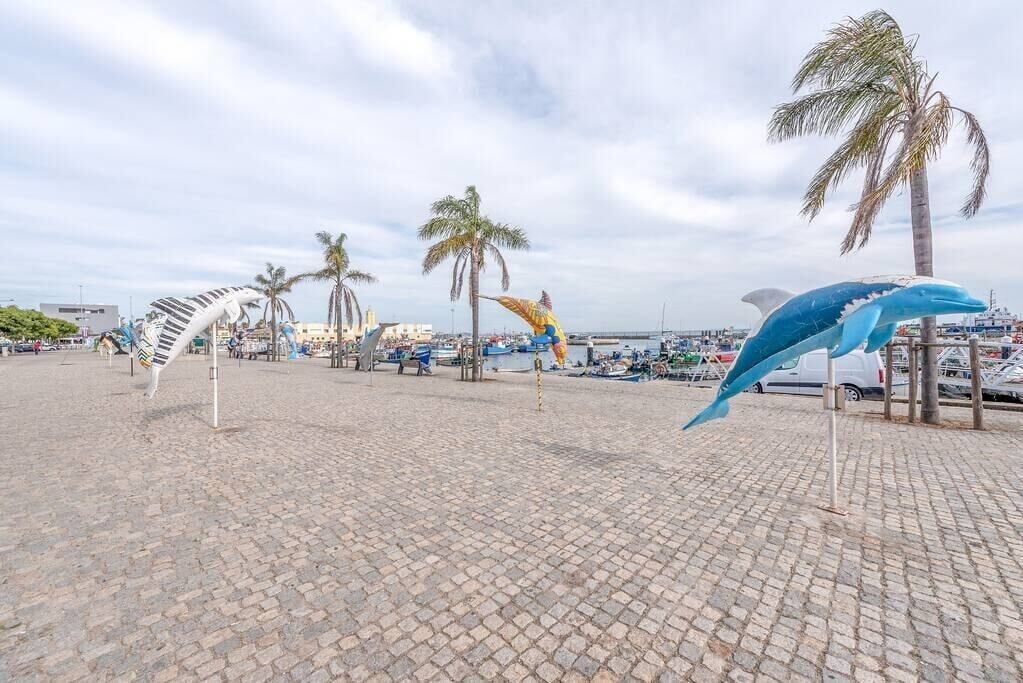 Una plaza adoquinada con palmeras y una escultura de delfín.