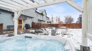 A backyard with a hot tub, wooden deck, and a covered patio area. - The Dancing Bears Den (Whitefish)