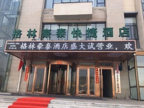 A hotel entrance with a red carpet, glass doors, and a signboard with Chinese characters.