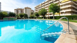 En swimmingpool med trappsteg som leder ner i vattnet, omgiven av en byggnad med flera balkonger och en klar himmel.