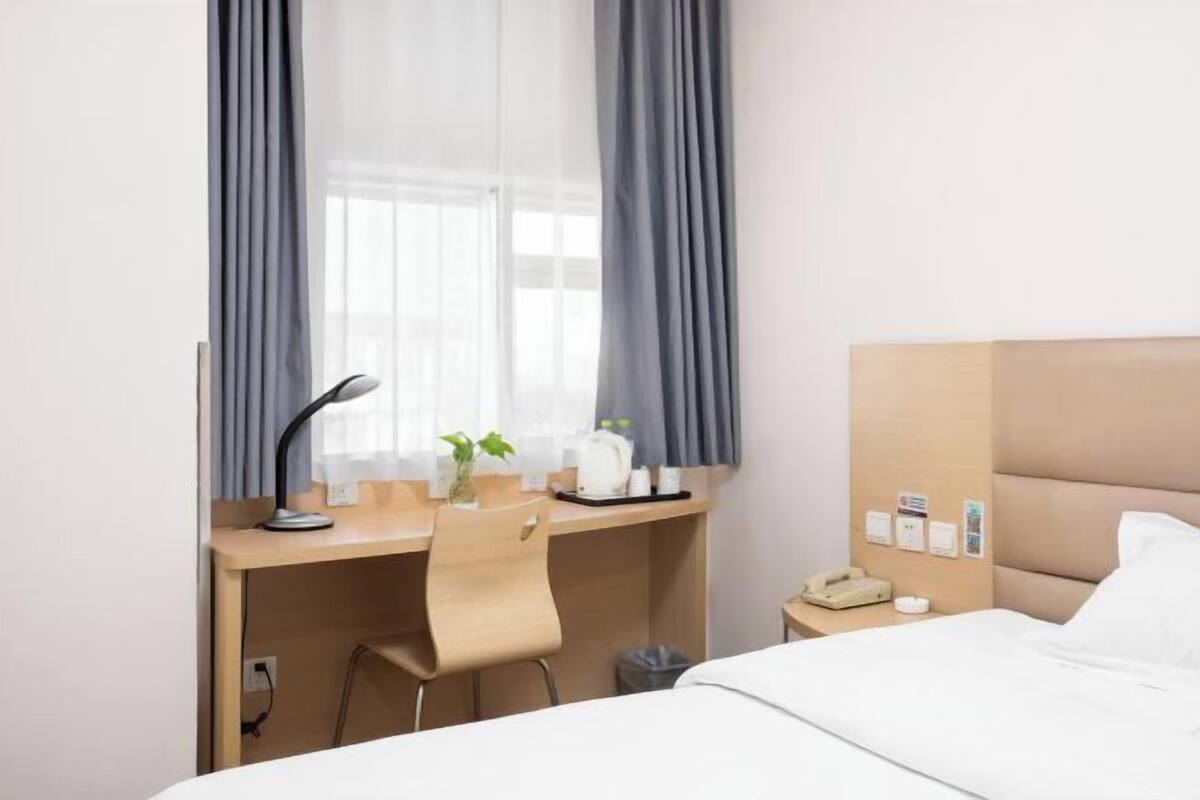 Hotellihuone, jossa on sänky, työpöytä tuolilla, puhelin ja ikkuna, jossa on verhot.