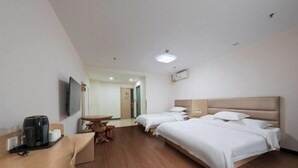 Une chambre d’hôtel avec deux lits, un bureau en bois avec une machine à café, une petite table et un téléviseur fixé au mur.