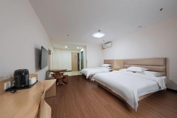 Habitación de hotel con dos camas, un escritorio de madera con cafetera, una mesita y un televisor montado en la pared.