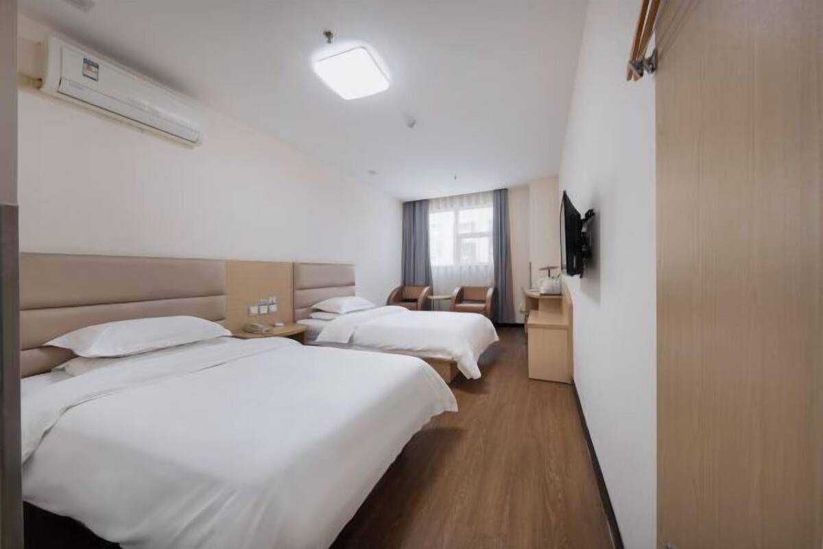 Hotellihuone, jossa on kaksi sänkyä, televisio, työpöytä ja ikkuna, jossa on verhot.