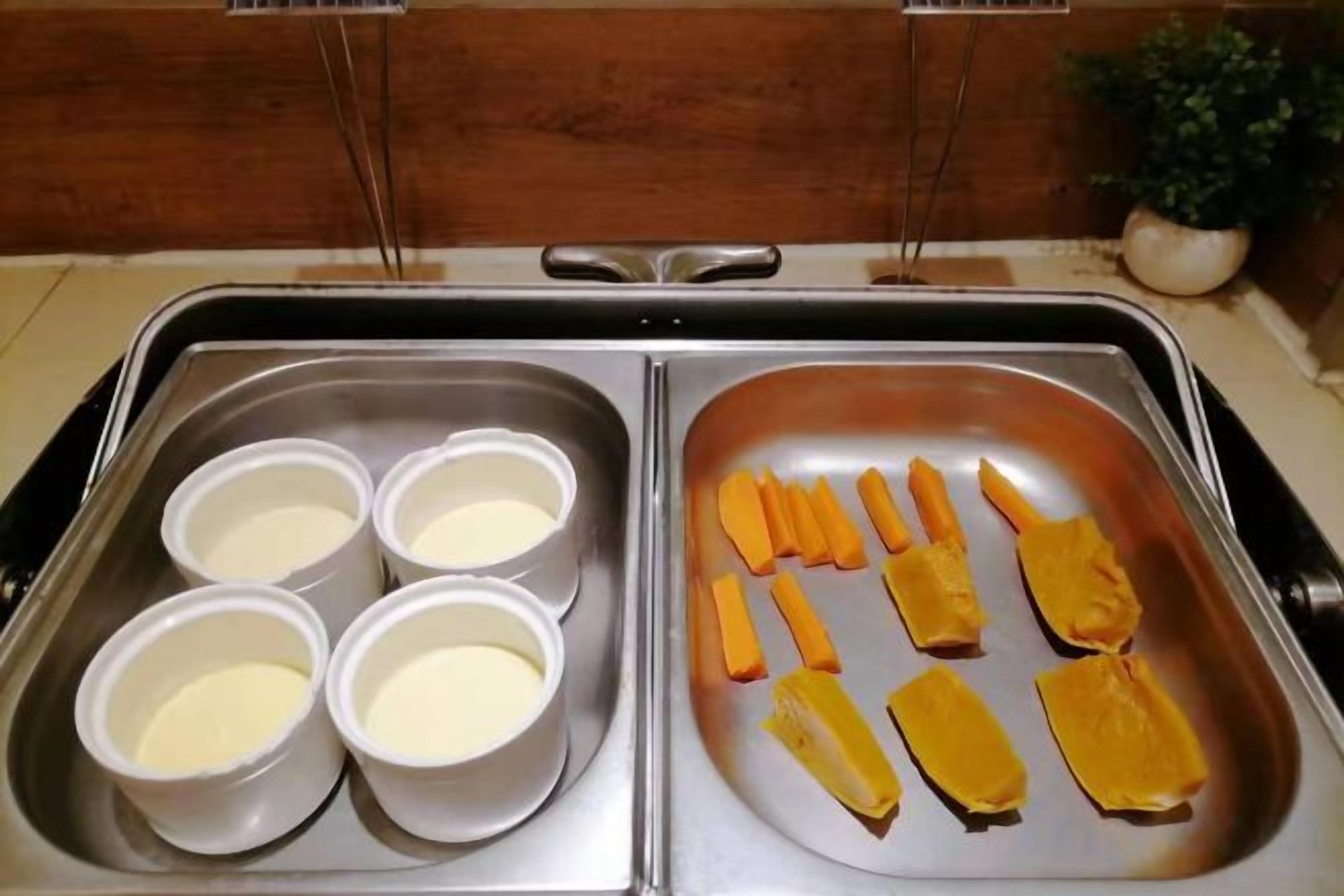 Bandeja de acero inoxidable con cuatro recipientes de sustancia blanca y varios trozos de comida amarilla.