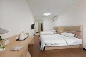 A hotel room with two beds, a desk with a kettle, a mirror, and a television on the wall.