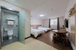 Habitación de hotel con ducha envuelta en vidrio, dos camas, una mesa de comedor de madera y un televisor montado en la pared.