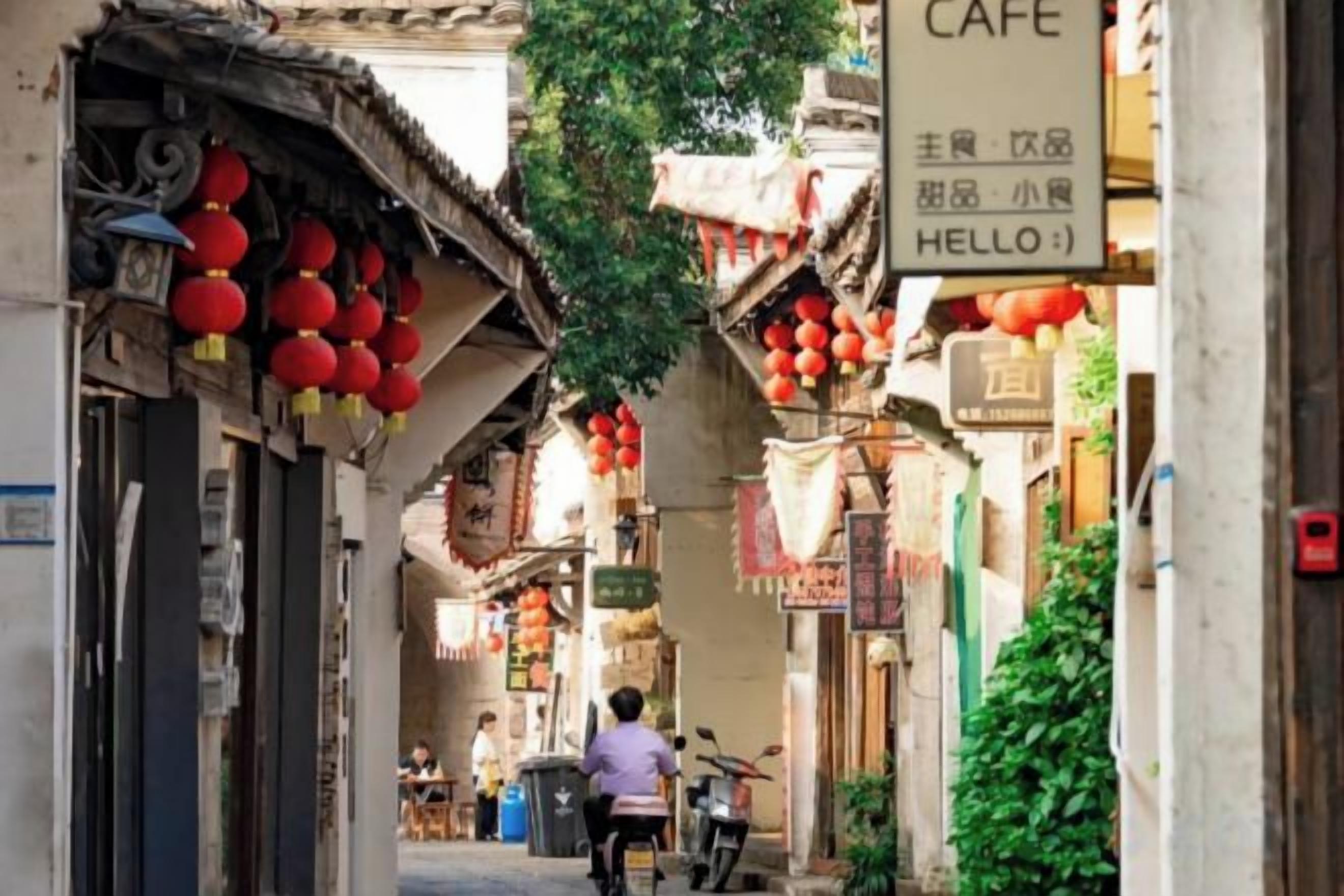 Une ruelle étroite aux bâtiments d’architecture traditionnelle, une enseigne de café et des lanternes rouges.