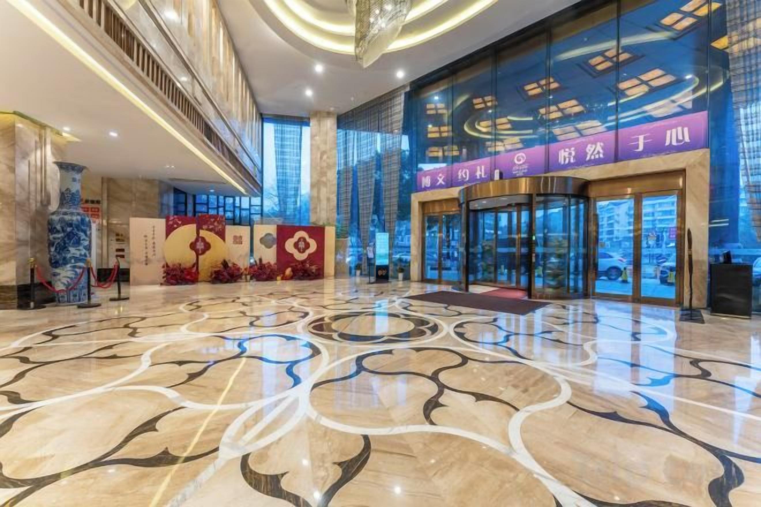 A hotel lobby with a marble floor, a reception area, and a glass entrance.