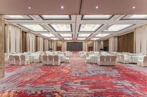Un salón de conferencias con mesas y sillas redondas, una alfombra estampada y un techo alto con tragaluces.