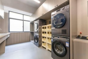 Lavandería con lavadoras y secadoras apiladas, una ventana y un estante con cestas de ropa.