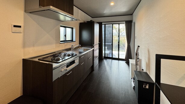 Een moderne keuken met een gasfornuis, oven en een RVS spoelbak. Boven de spoelbak is een raam en er is een schuifpui naar een balkon.