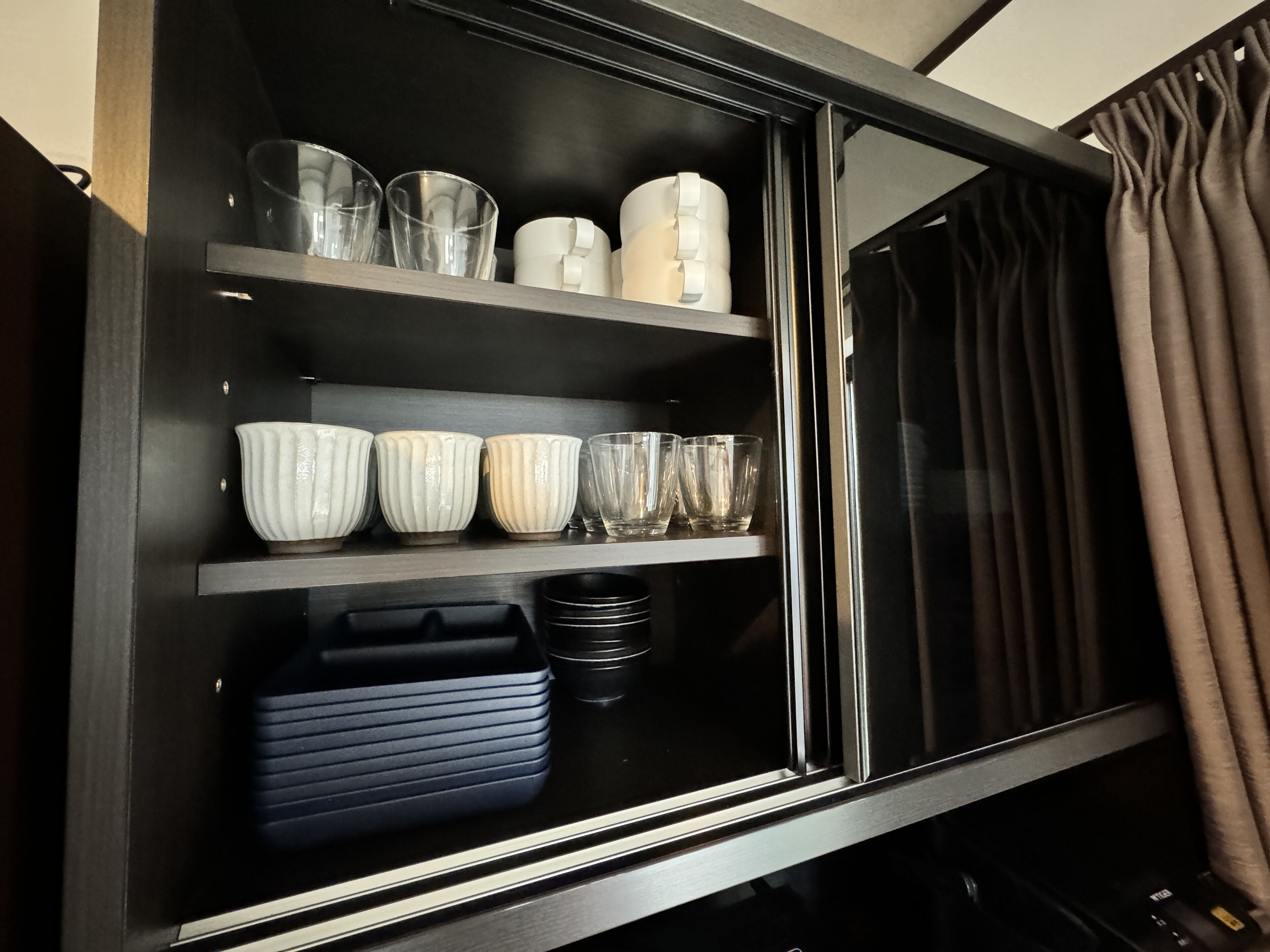 A black-framed cabinet with shelves holding clear glasses, white bowls, and black plates.