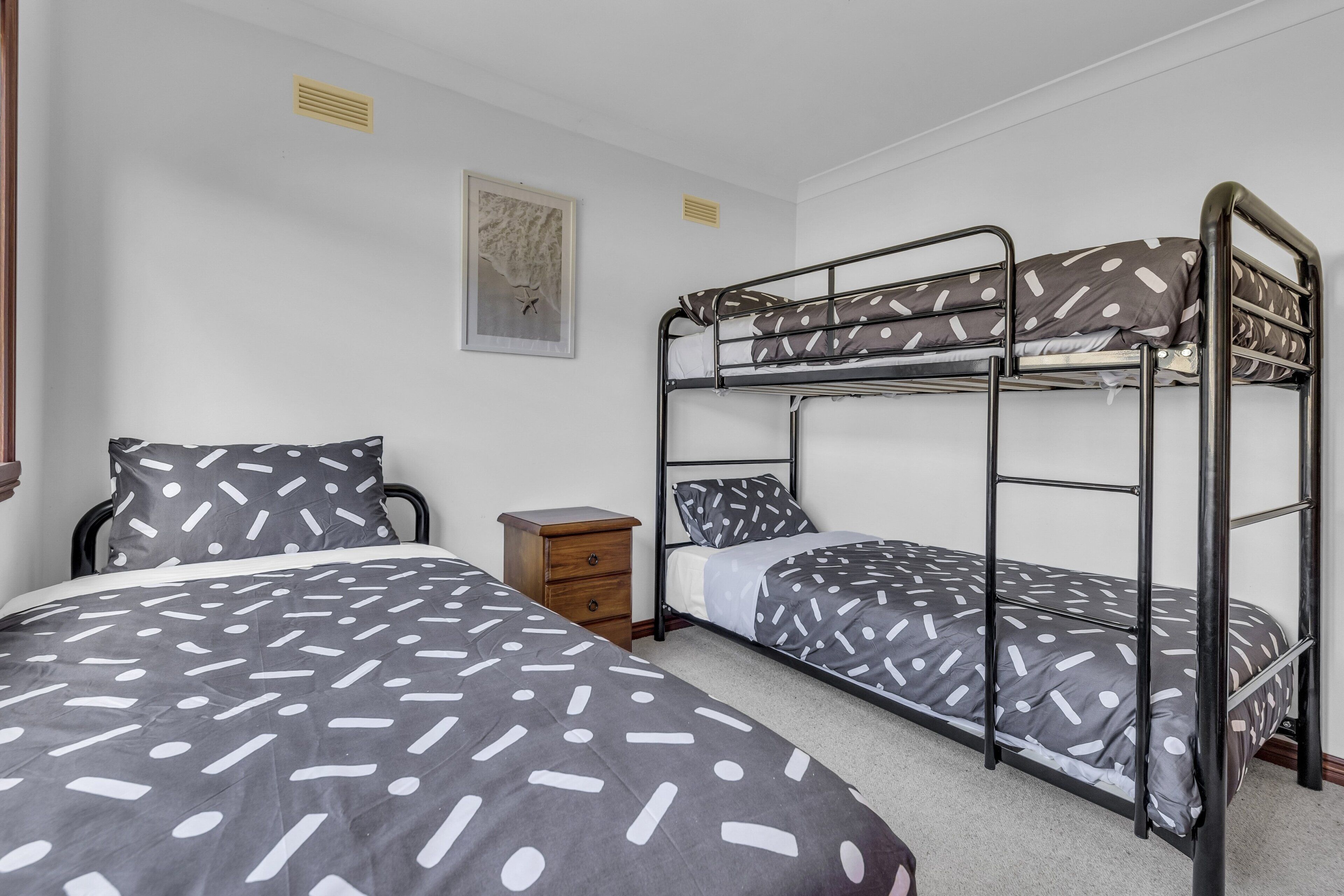 A bunk bed room with a patterned bedspread, a small wooden nightstand, and a framed picture on the wall.