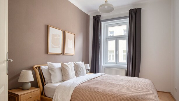 A bedroom with a bed, bedside tables, a window with curtains, and framed pictures on the wall.
