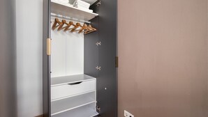 A walk-in closet with open doors, featuring a grey wardrobe, a white shelf with folded towels, and wooden hangers on a rod.