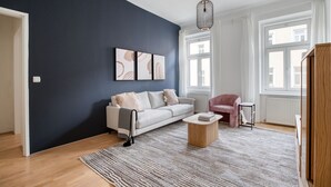 A modern living room with a dark blue accent wall, a white sofa, a pink armchair, and a wooden coffee table.